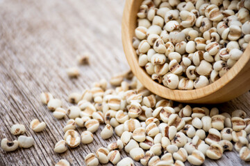 White Job's tears ( Adlay millet, pearl millet or coix seeds ) in wooden bowl  isolated on wood table background. 