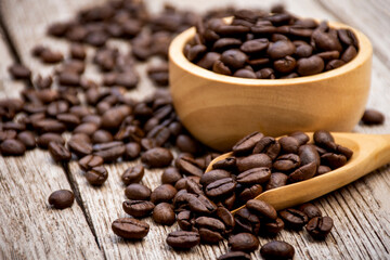 coffee beans in a wooden scoop and bowl on wooden table.
