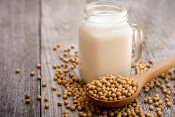 Glass jug of soy milk with soy beans isolated on wood table.