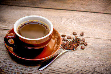 Red cup of coffee with beans on wood table background.