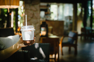 Closeup of woman's hand showing a cup of cold chocolate in coffee shop.Select focus on the glass