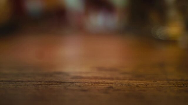 A person putting down a  delicious glass of whiskey. Detail shot of a hand putting down and picking up a glass of whiskey on a wooden table.