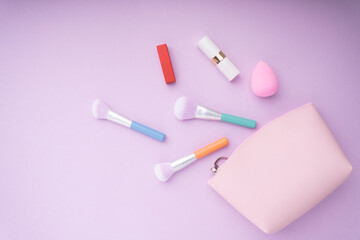 Cosmetic pastel colourful accessories in pink tone over purple pink background.