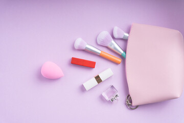 Cosmetic pastel colourful accessories in pink tone over purple pink background.