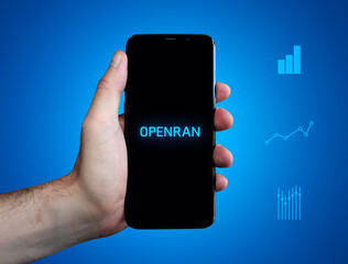 openRAN. Hand hält Telefon (Handy). Wort auf Display. Diagramme auf Hintergrund blau. Business