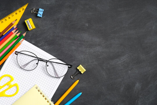 Back to school concept. School stationery, glasses, paper notebook on black board background. Flat lay, top view, overhead.