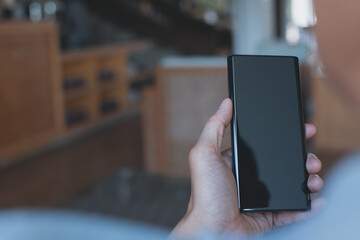 Mockup of man hand holding and looking at black blank screen mobile phone at home