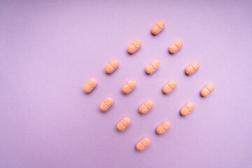 Top view - Orange pills over purple pink background. Square shape.