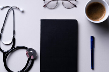 Top view - Doctor working table with stethoscope, tablet, pen, and eyeglasses over grey background.