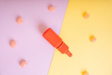 Top view - Orange bottle contain lipstick brush over yellow and purple background with candy.