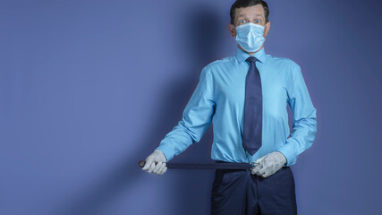 Businessman in a medical mask and medical gloves tightens a belt on his pants, isolated on background. Business crisis during a pandemic.