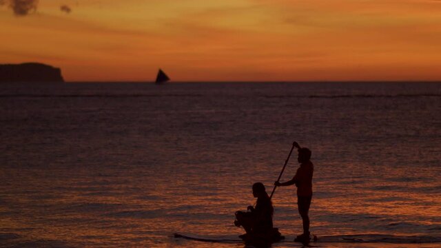 Artistic Reveal Shot Of Two People On Paddle Boat While In Silhouette Of Sunset