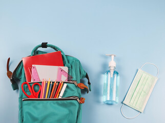 COVID-19 prevention while going back  to school  and new normal  concept. Top view of backpack with school supplies , surgical mask and sanitizer gel on blue background