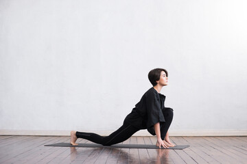 Young and fit woman practicing yoga indoor in the class. Stretching exercise in the day light. Sport, fitness, health care and lifestyle.