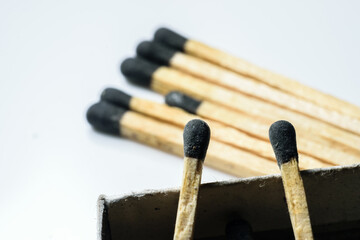 Two match sticks in focus over the edge of a match box and multiple match sticks laying on the floor in the background. White background
