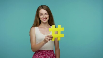 Lovely blogger girl in summer dress holding hashtag symbol, pointing at copy space, empty advertising area for commercial text, viral tagged internet message. studio shot isolated on blue background
