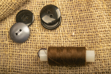 Different buttons and a spool of thread on the burlap with a rough texture. Close up.