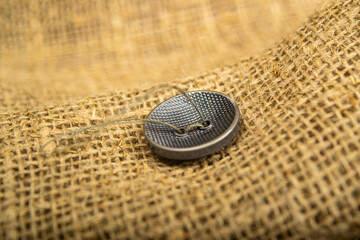 A black button sewn to a piece of burlap. Close up.