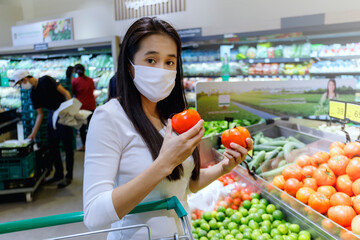 Asian woman wearing protective face mask push and hold shopping cart in supermarket department store. Girl, looking grocery to buy  some food. New normal after covid-19. Family concept.