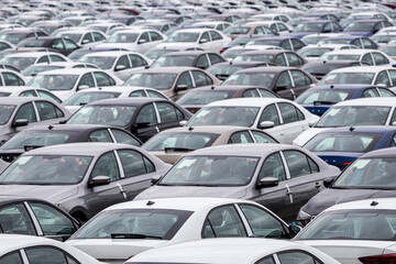 Rows of a new cars parked in a distribution center on a car factory on a cloudy day. Top view to the parking in the open air. © Eugene_Photo