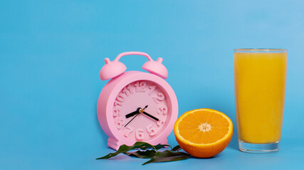 Closeup pink alarm clock with glass of orange juice and fresh ripe fruit on a blue background....