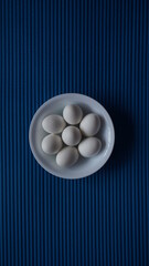 White eggs in a white dish with a blue texture background 