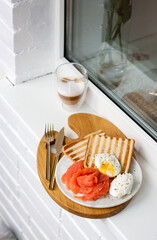 Breakfast menu: toasted bread, smoked salmon, poached eggs and cup of coffee on white windowsill