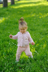 Little girl in casual clothes makes her first steps on the grass.