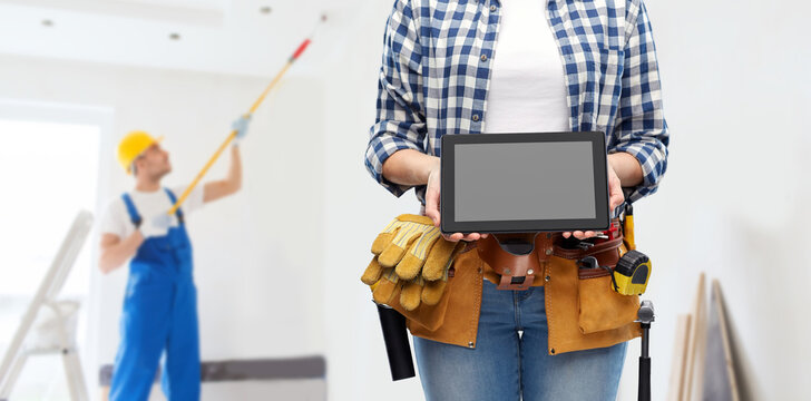 repair, construction and building concept - woman or builder with working tools on belt showing tablet pc computer over painter painting ceiling background