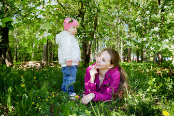 Portrait of young mother and her small daughter in the park full of apple blossom trees in a spring day. Woman and girl in nature landscape