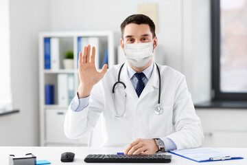 healthcare, medicine and people concept - male doctor in medical mask with stethoscope waving hand at hospital