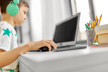 technology, gaming and people concept - boy in headphones playing video game on laptop computer at home