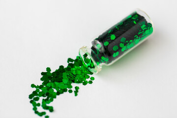 party, decoration and holidays concept - green hexagonal glitters poured from small glass bottle...