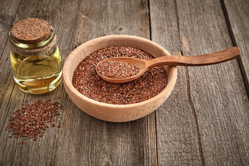 Flax seeds and a wooden spoon on a wooden table. Wooden bowl with bottle of oil. Healthy food and drink concept.