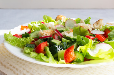 Fattoush salad of vegetables and toasted pita bread in a white plate with a napkin on a light background. Close up. Summer vegetarian salad