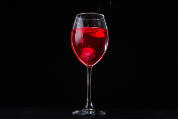A glass of red vine on black background. Wine glass on dark table. Falling ice cubes and splashes