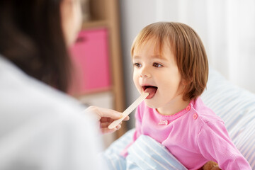 healthcare, medicine and people concept - doctor checking sick little girl's throat with tongue...