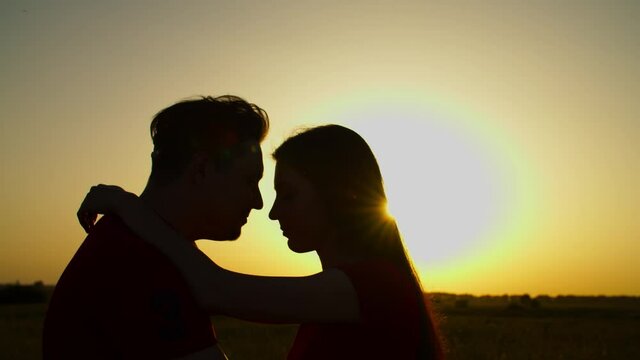 Silhouette of passionate couple standing face to face, bonding , embracing, caressing and kissing in rays of summer sundown, expressing affection, happiness and unity.