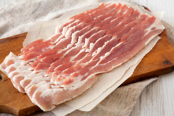 Uncooked Raw Bacon on a rustic wooden board on a white wooden background, side view. Close-up.