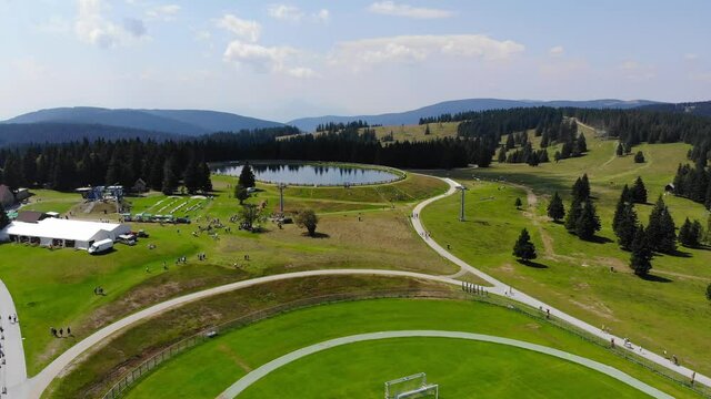 Trails in Rogla sports resort Slovenia during springtime passing around a small lake near a soccer field, Aerial flyover shot