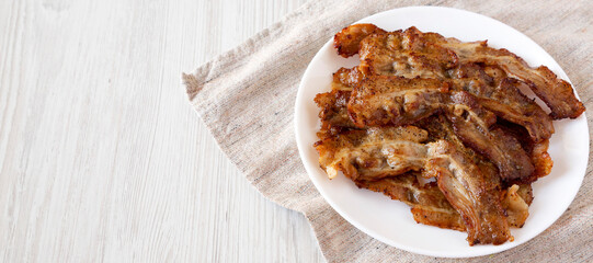Homemade Fried Bacon on a white plate on a white wooden table, low angle view. Copy space.