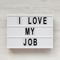 'I love my job' on a lightbox on a white wooden surface, top view. Flat lay, from above, overhead. Close-up.