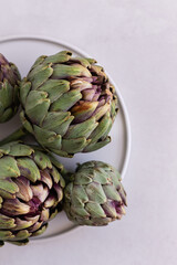 Obraz premium Topview image of artichokes in a white plate over light gray bac