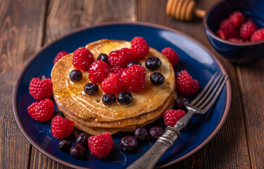 Sliced sweet homemade pancakes with raspberries and blueberries on blue plate.