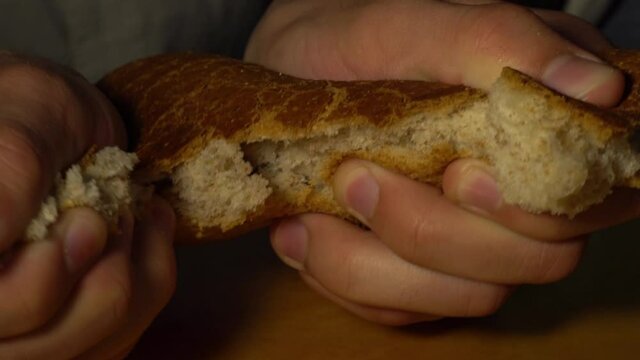 Caucasian man baker tears rye baguette into two parts. Close-up of a breaking bread.