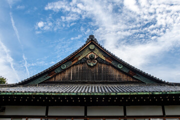 Fototapeta na wymiar Wooden, richly decorated Nijo Castle roof in Kyoto, with golden ornaments, Japan. Blue sky in the background, symmetrical view. 