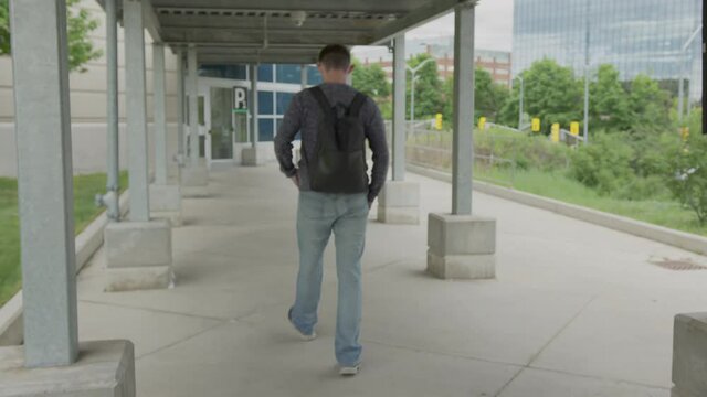 High quality 4k video of a young men who is walking outside on the street to to from parking lot on the train station. Canada GO train and bus station. Handsome men carrying backpack