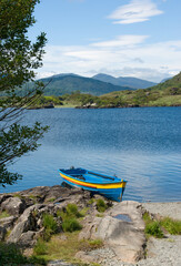 Little blue fishing boat, beached beside a holly tree on the shore of the Upper Lake, Killarney, Ireland, on a peaceful summer's day