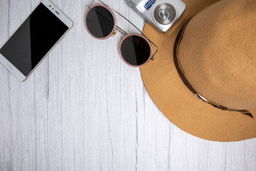 Traveler accessories, luxury hat, sun glasses, camera and smart phone on white white wood background with copy space. Travel vacation concept. Summer background. Flat lay, top view.