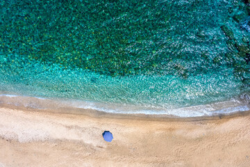 Fototapeta na wymiar An umbrella on a empty beach with emerald and turquoise sea at the Aegean Islands of Greece, Andros